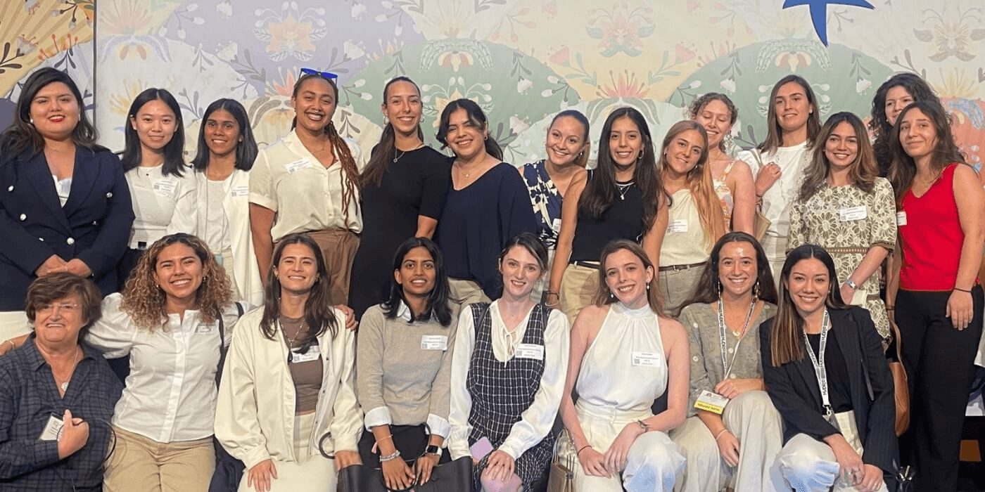 A group of diverse women posing together in front of a floral wallpaper.