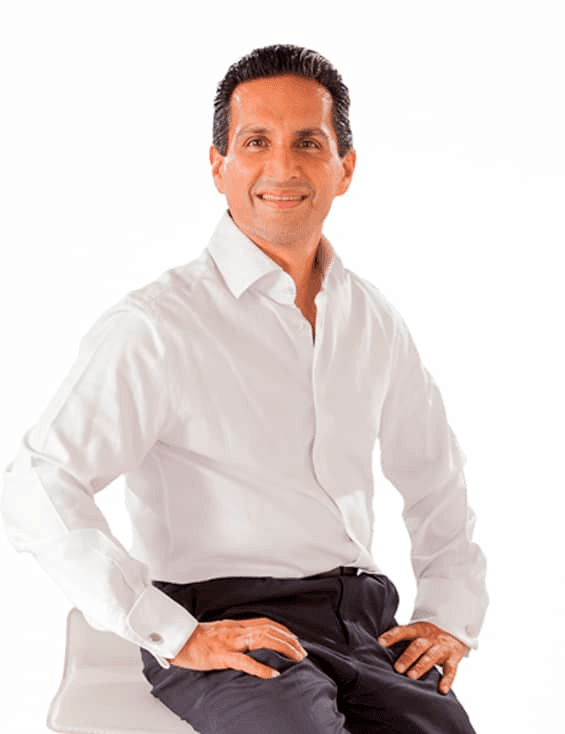 A man in a white shirt and black pants sitting on a white chair against a white background.