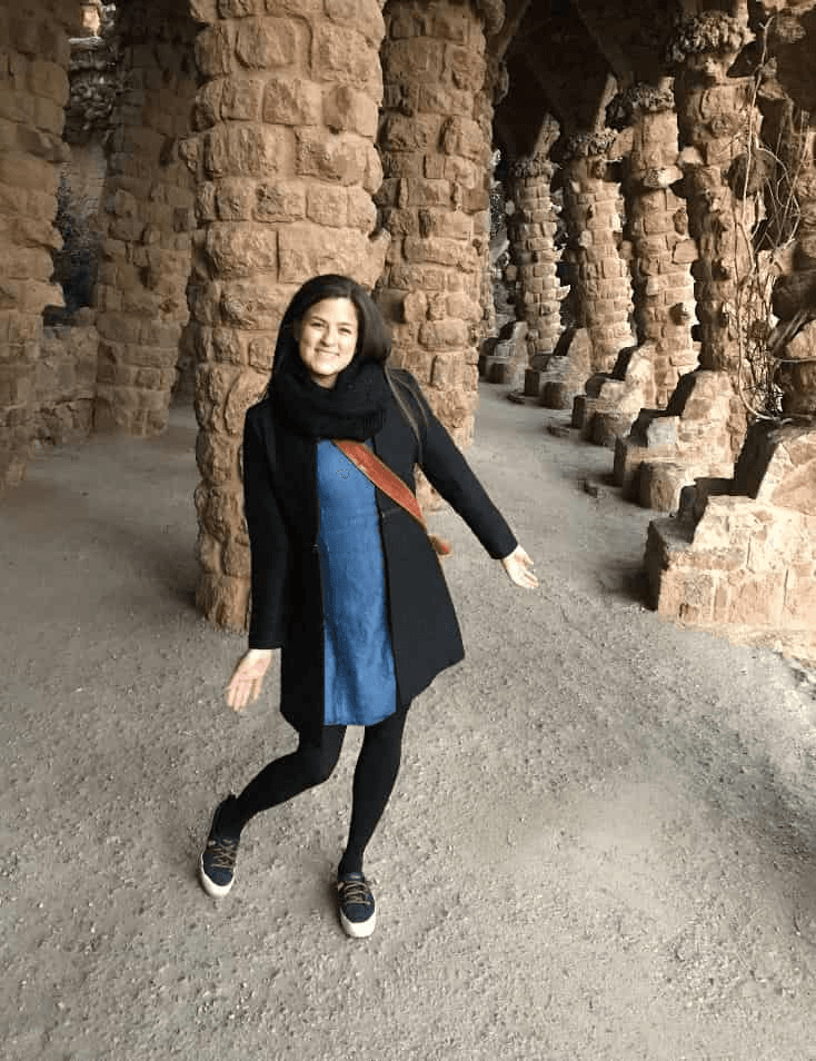 A woman smiling and posing between tall stone columns in an ancient, historical site.
