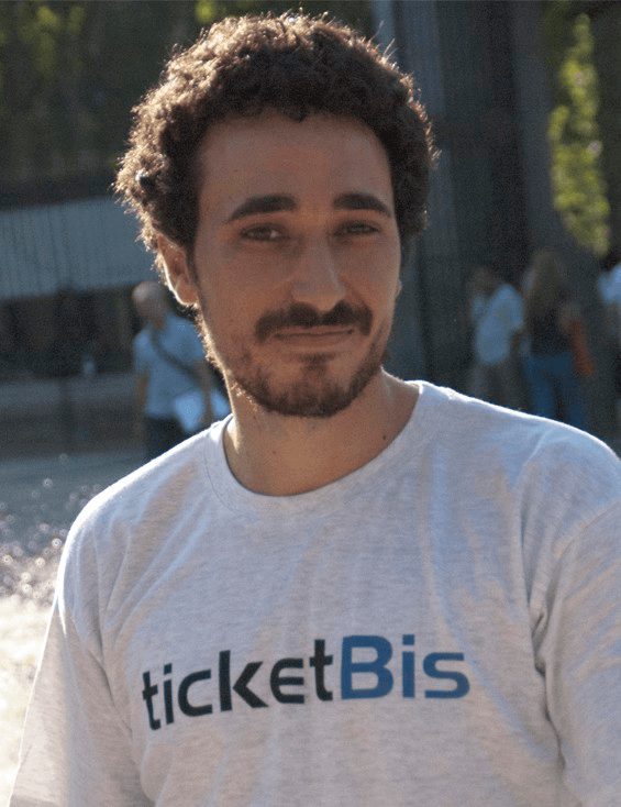 A man with curly hair wearing a 'ticketBis' T-shirt is smiling at the camera.