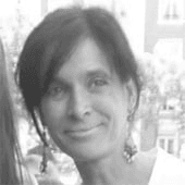 Black and white photo of a smiling woman with shoulder-length hair and earrings, standing outdoors.