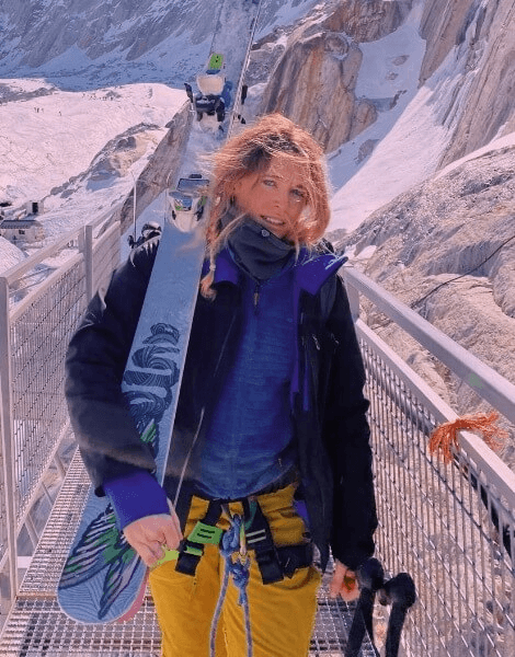 A person holding a snowboard on a bridge with icy mountain background.