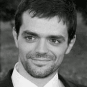 A black and white photo of a smiling man in a suit.