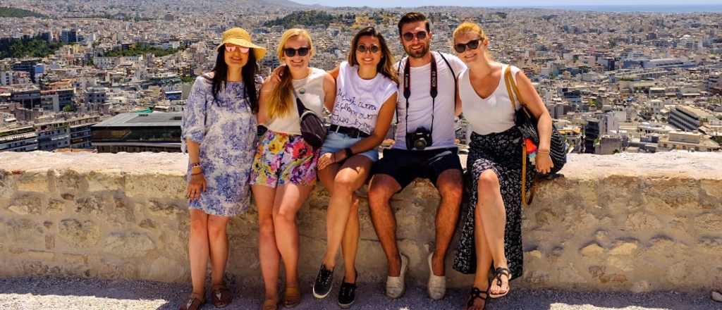 Five people sitting on a stone wall with a panoramic view of a city in the background.