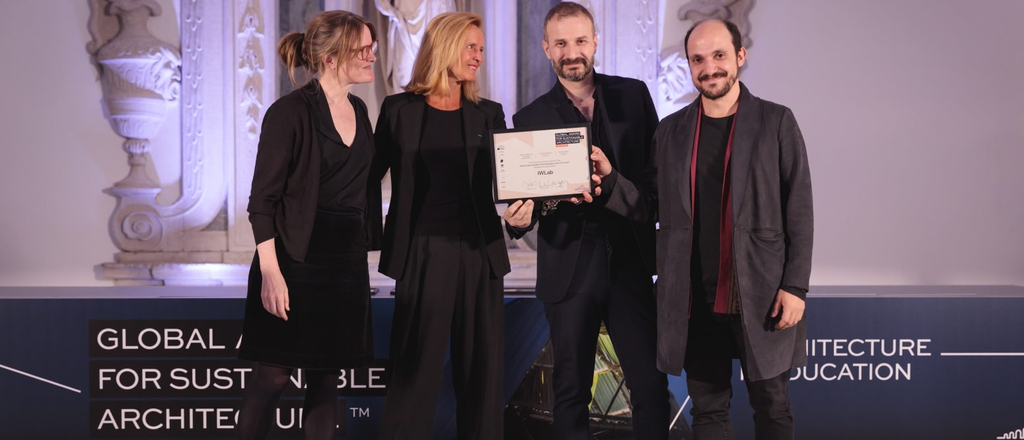 Four people standing on stage, one of them holding an award certificate, at a sustainable architecture event.