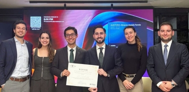 A group of six individuals standing together, smiling while holding a certificate in an indoor setting.