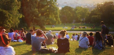 A crowd of people sitting on a grassy hill during sunset.