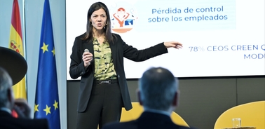 A woman presents at a corporate event with a projection screen displaying text about employee management, as attendees listen.