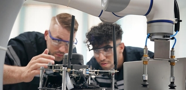 Two men are closely examining a robotic arm and its mechanisms in a lab setting.