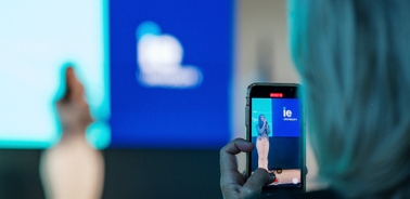 A person is taking a photo of a speaker at an event with a smartphone.