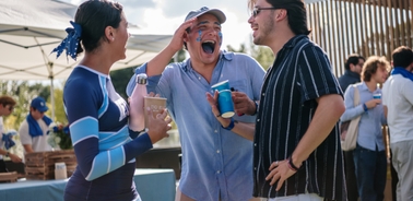 Three young adults are enjoying drinks and laughing together at an outdoor gathering.