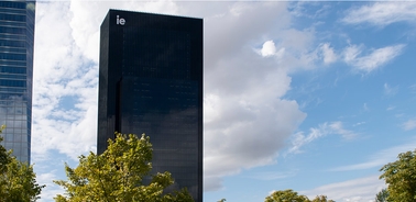 A modern black skyscraper stands prominently against a blue sky with scattered clouds.
