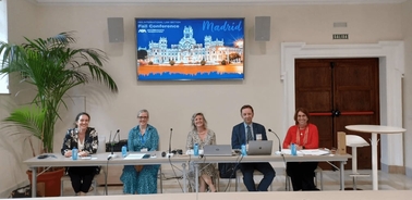 Five individuals sitting at a conference table in a room with a 'Madrid' digital display in the background.