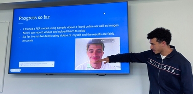 A man presenting a facial recognition project on a digital screen in a classroom.