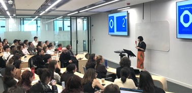 A speaker presents to an engaged audience in a modern classroom setting.