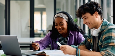 Two students are studying together at a table with a laptop open.