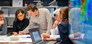 A group of professionals collaborating around a table with documents and a laptop.