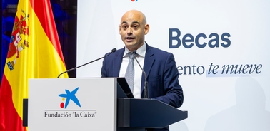 A man speaking at a podium with logos of 'Fundación la Caixa' and a sign that says 'Becas' during a formal event.