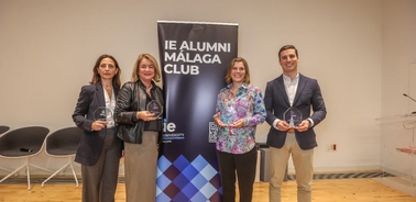 Four people standing together holding awards in front of an IE Alumni Málaga Club banner.