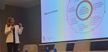 A woman giving a presentation in a conference room with a slide titled 'Mejores prácticas' projected on a screen.