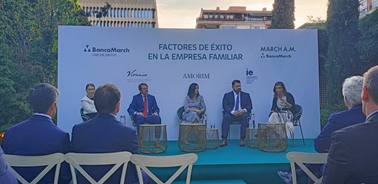 A panel discussion at an outdoor event with five speakers seated in front of an audience.