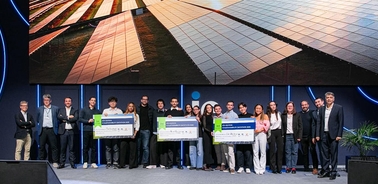 A group of people standing together on stage with large checks, showcasing a solar panel background.