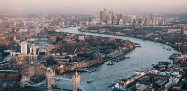 Aerial view of London showing the River Thames, Tower Bridge, and skyscrapers in the financial district during sunset.