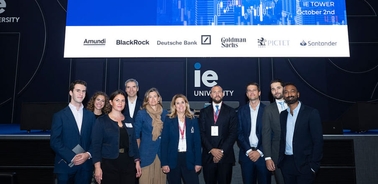 Group of professionals posing on a stage with corporate logos in the background at a university event.