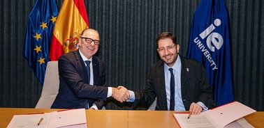 Two men are shaking hands in a formal setting, with flags in the background.