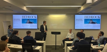 A business meeting in a conference room with a presenter and several attendees focusing on projection screens.