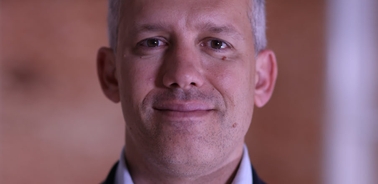 Close-up of a middle-aged man with a slight smile, looking directly at the camera