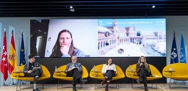 A panel discussion taking place with several speakers and a virtual participant displayed on a screen.