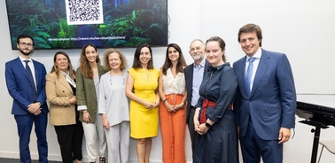 A group of nine people, possibly professionals, posing for a photo in a room with a QR code displayed on a screen behind them.