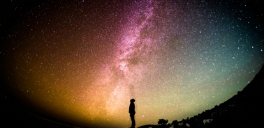 A silhouette of a person standing against a vibrant night sky filled with stars and the Milky Way.