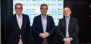 Three men smiling for a photo in front of a backdrop with multiple logos, including 'ONCE'.