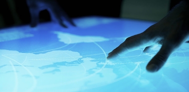 A person's hands interact with a glowing map on a touchscreen surface.