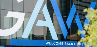 The image shows a glass facade of a building with the word 'GAM' and the phrase 'WELCOME BACK HOME' displayed prominently.