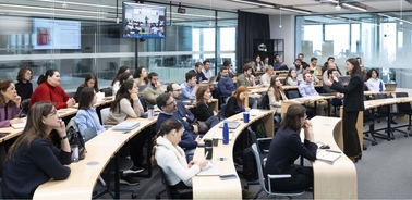 A group of students attentively listening to a speaker in a modern classroom setting.