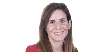 A portrait of a smiling woman with long brown hair wearing a red top against a white background.