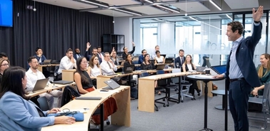 A diverse group of professionals engaged in a modern classroom setting, with one man leading the discussion.