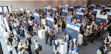 A large crowd of people engaged in a career fair with various booths.