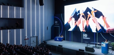 The image depicts a graduation ceremony with students celebrating by tossing their caps in the air.