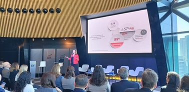 A woman presenting a business slide to an audience in a modern conference room.