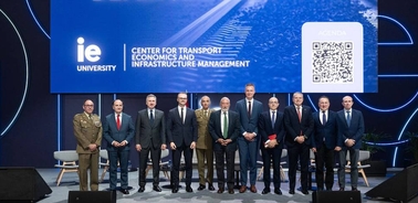 A group of men in business attire standing on a stage at an event related to transport economics and infrastructure management.