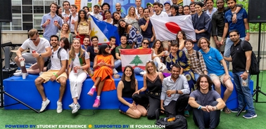 A group of cheerful students from diverse backgrounds poses with flags at an outdoor event.
