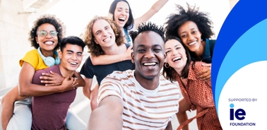 A group of diverse young adults smiling and taking a selfie together outdoors.