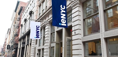 A view of a city street with large blue flags displaying 'ieNYC' hanging from a modern building facade.