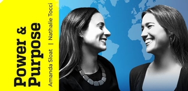 Two women smiling at each other with a world map in the background.