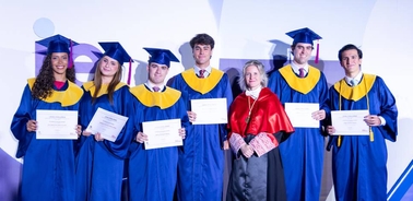 A group of graduates in blue gowns and caps holding diplomas at a graduation ceremony.
