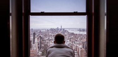 A person gazing out a window at a panoramic city skyline.